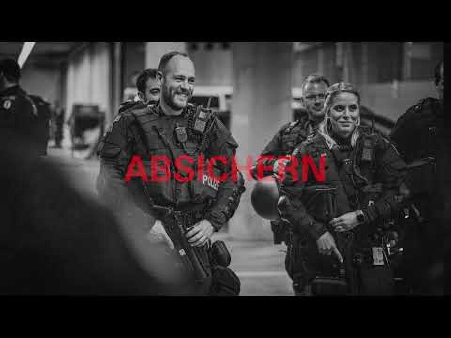 Eine Gruppe bewaffneter Polizisten lächelt und unterhält sich. Das Bild ist in Schwarz-Weiß gehalten, in der Mitte steht in fetter roter Schrift „ABSPICKEN“.