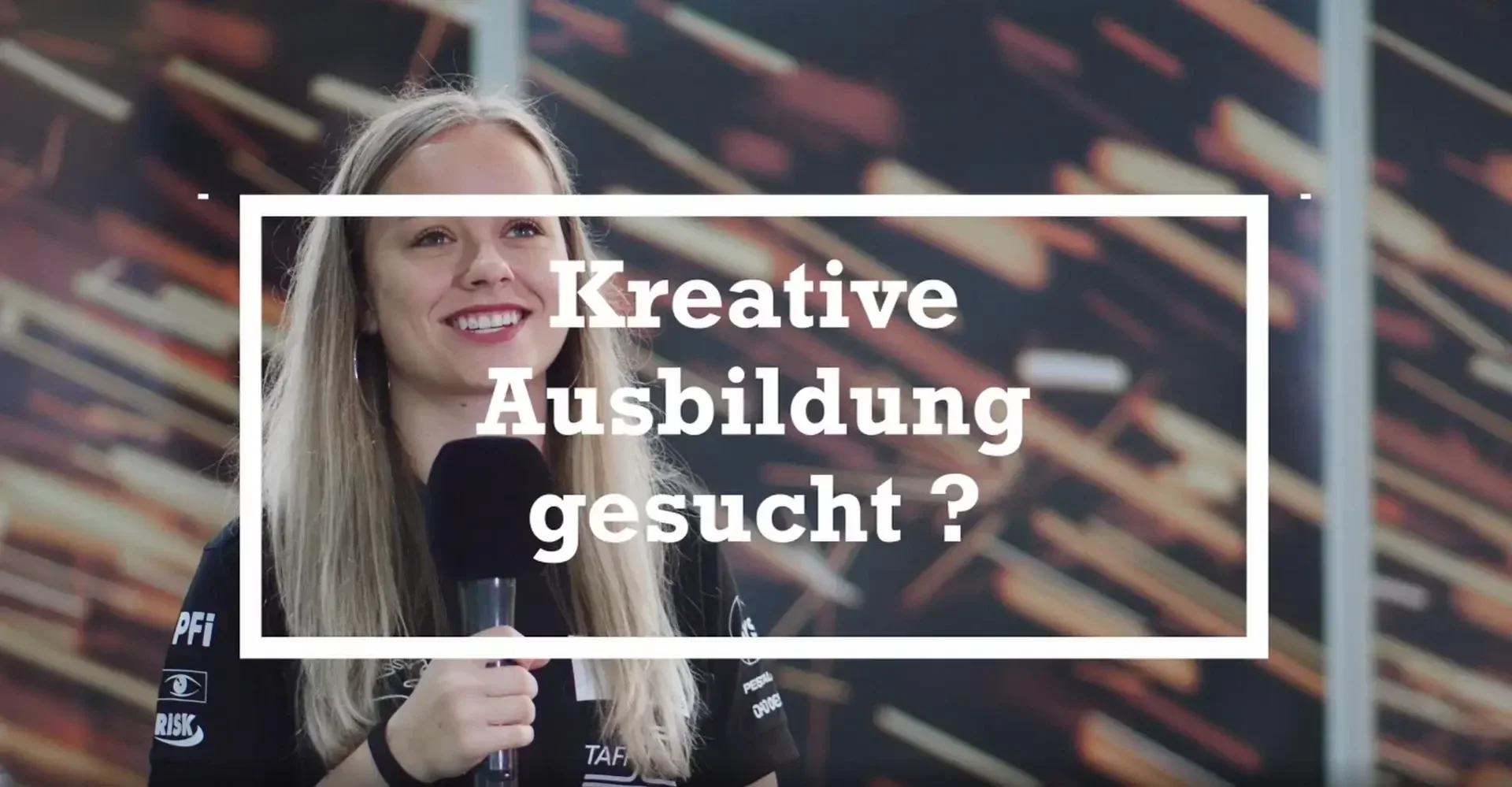 Eine lächelnde Frau hält ein Mikrofon in der Hand. Der eingeblendete Text auf Deutsch lautet: „Kreative Ausbildung gesucht?“ Im Hintergrund ist ein abstraktes Muster zu sehen.