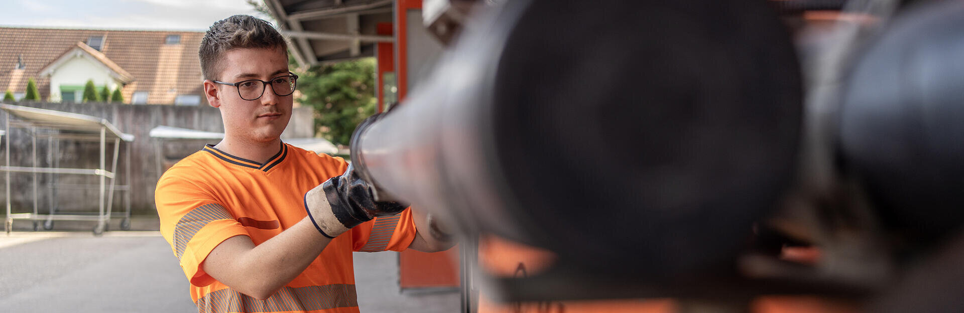 Eine Person, die ein orangefarbenes Sicherheitshemd und Arbeitshandschuhe trägt, bedient eine Maschine.