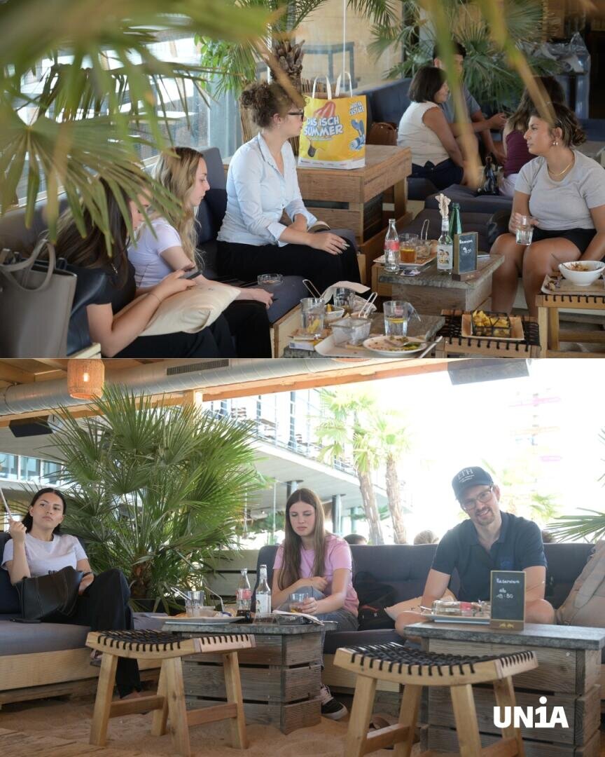 Zwei Fotos von jungen Erwachsenen, die in einem modernen Straßencafé auf Sofas sitzen, sich unterhalten und essen. Auf dem Tisch stehen Speisen, Getränke und Taschen. Sie sind von Palmen und Holzdekorationen umgeben. Die Atmosphäre ist entspannt und gesellig.